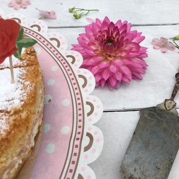 Kuchenkante auf rosa Papier mit pinker Dahlie und Tortenheber auf hellem Holz