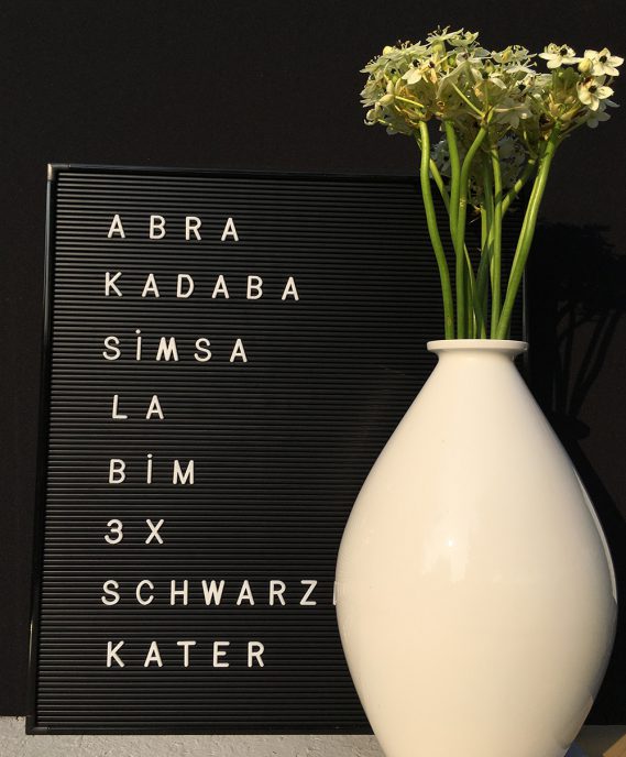 Letterboard mit zauberspruch und weißer Vase mit weißen Blumen