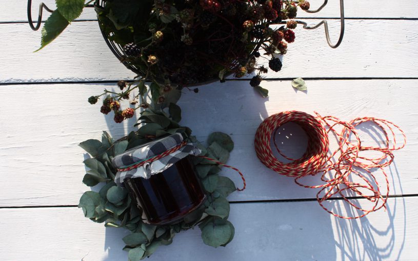 Blick auf Brombeeren in Sieb, auf Marmeladenglas und rote Kordel