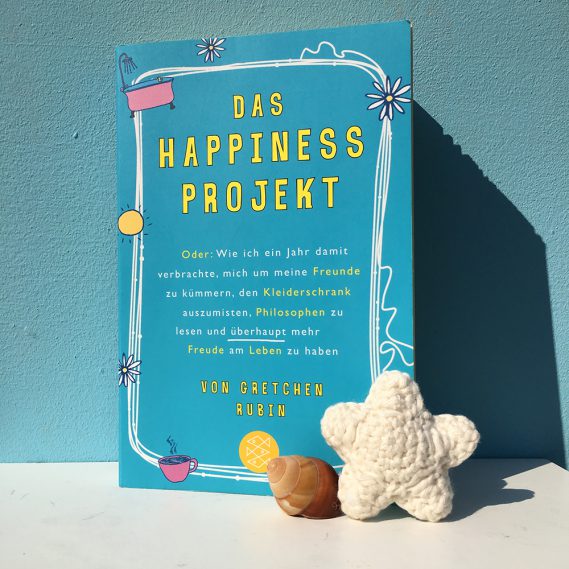 Das Happiness Projekt mit Häkelstern und Muschel vor blauem Hintergrund