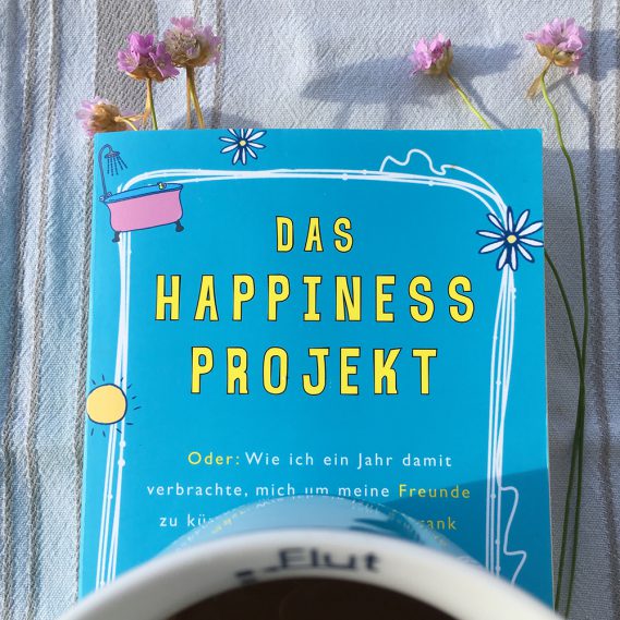 Das Happiness Projekt, nah mit Kaffeetasse und lila Strandblumen