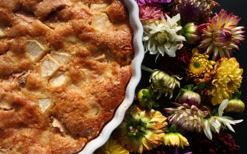 Goldbrauner Apfelkuchen von oben mit verblühten Dahlien auf schwarzem Untergrund