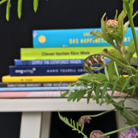 Bücherstapel verschwommen auf weißem Hocker vor schwarzem Hintergrund mit rankenden Blumen scharf