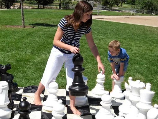 Two children and playing with giant chess pieces on a lawn outdoors