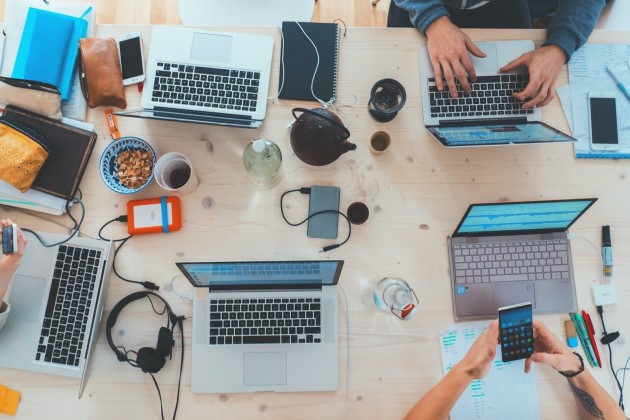 Grupo de pessoas reunidas em uma mesa.  Imagem mostrando os computadores e acessórios. 