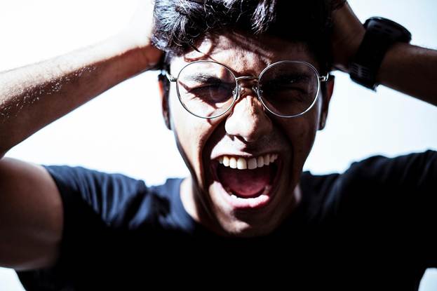 A man is visibly very frustrated and screaming with his hands on the top of his head