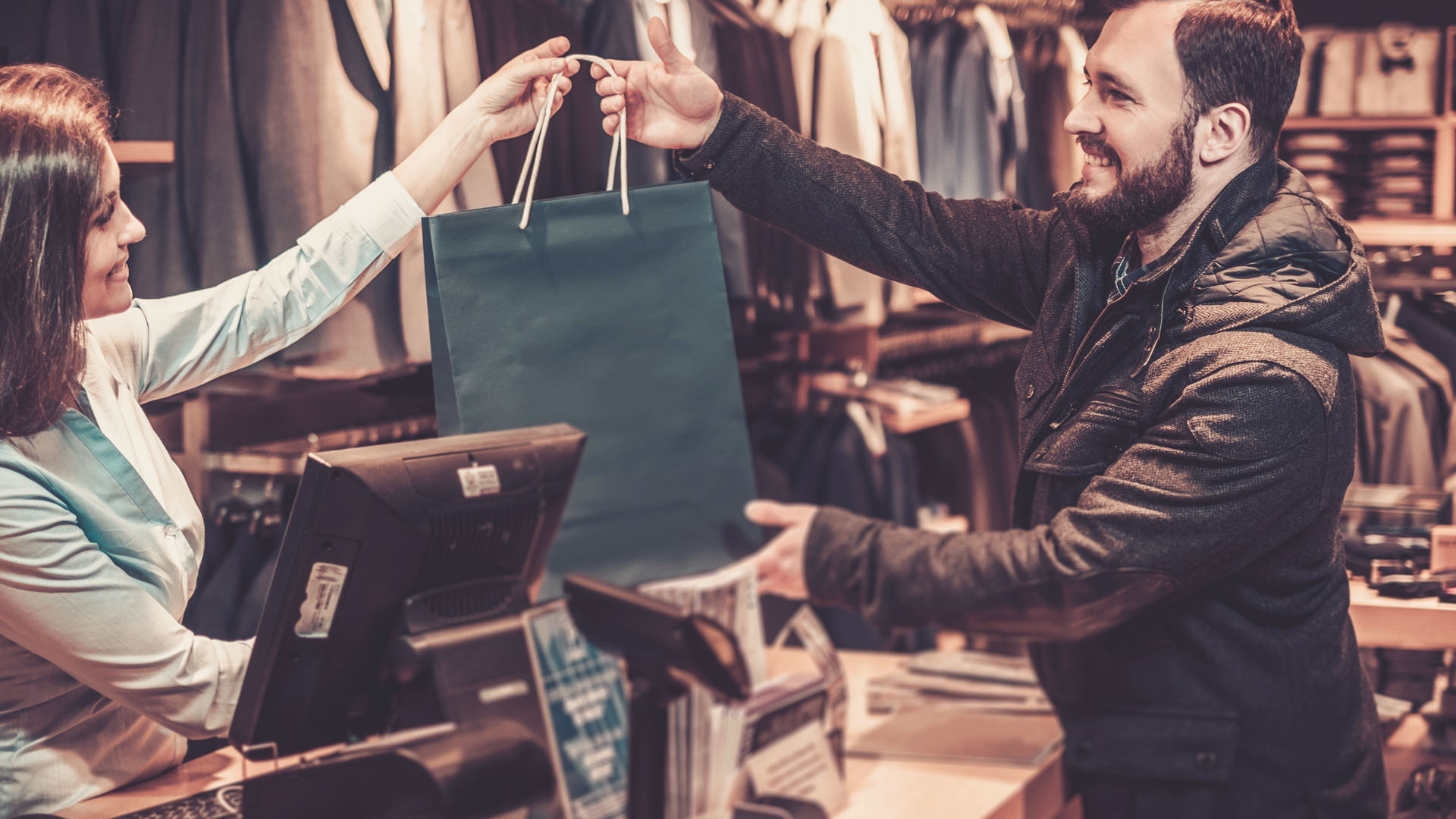 Vendedor oferece um produto a uma cliente em loja de roupas.