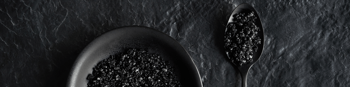 Black salt in a bowl with spoon on slate board