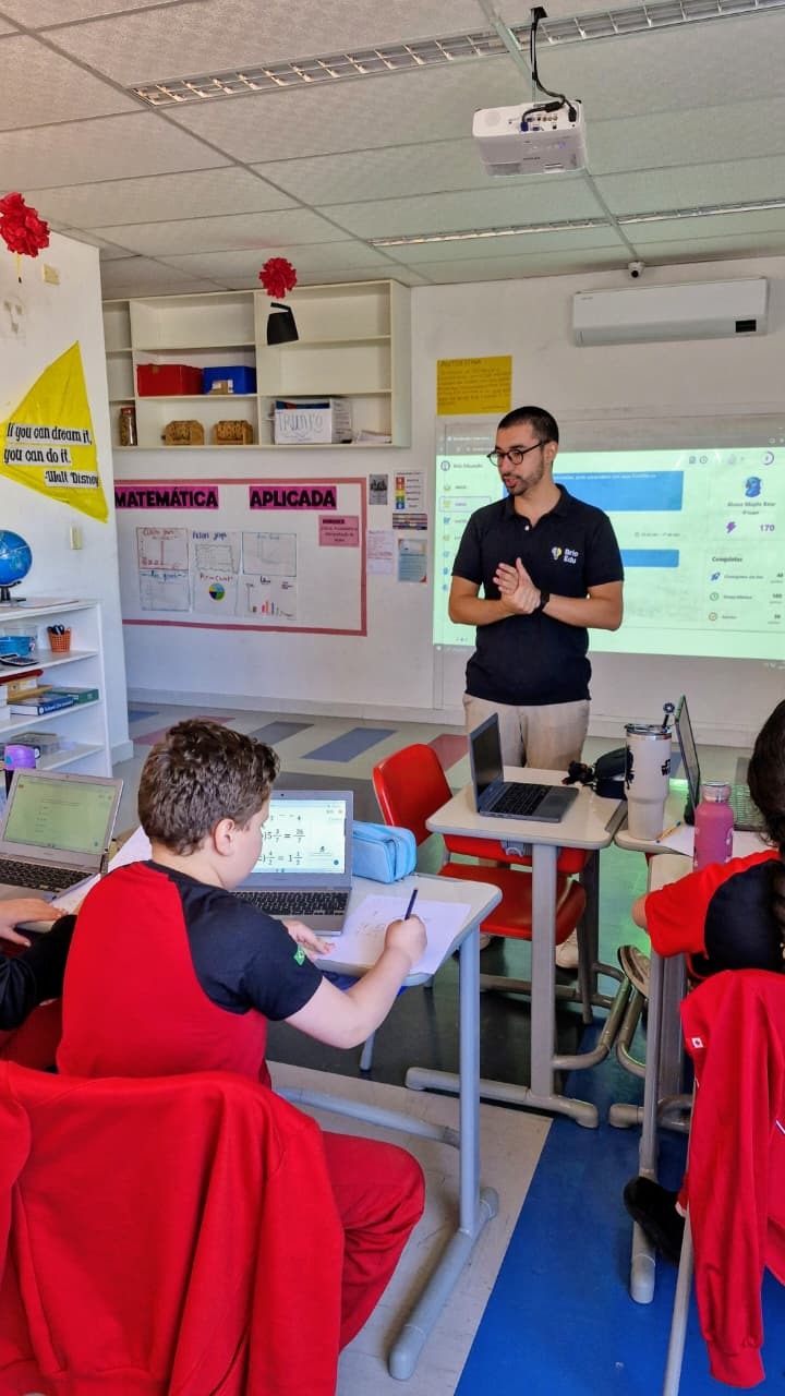 Sala de aula com professor e tela da Brio projetada, alunos com notebooks
