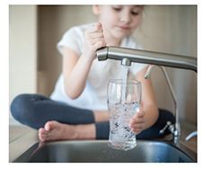 Lifestyle photo of girl drawing water from a kitchen faucet