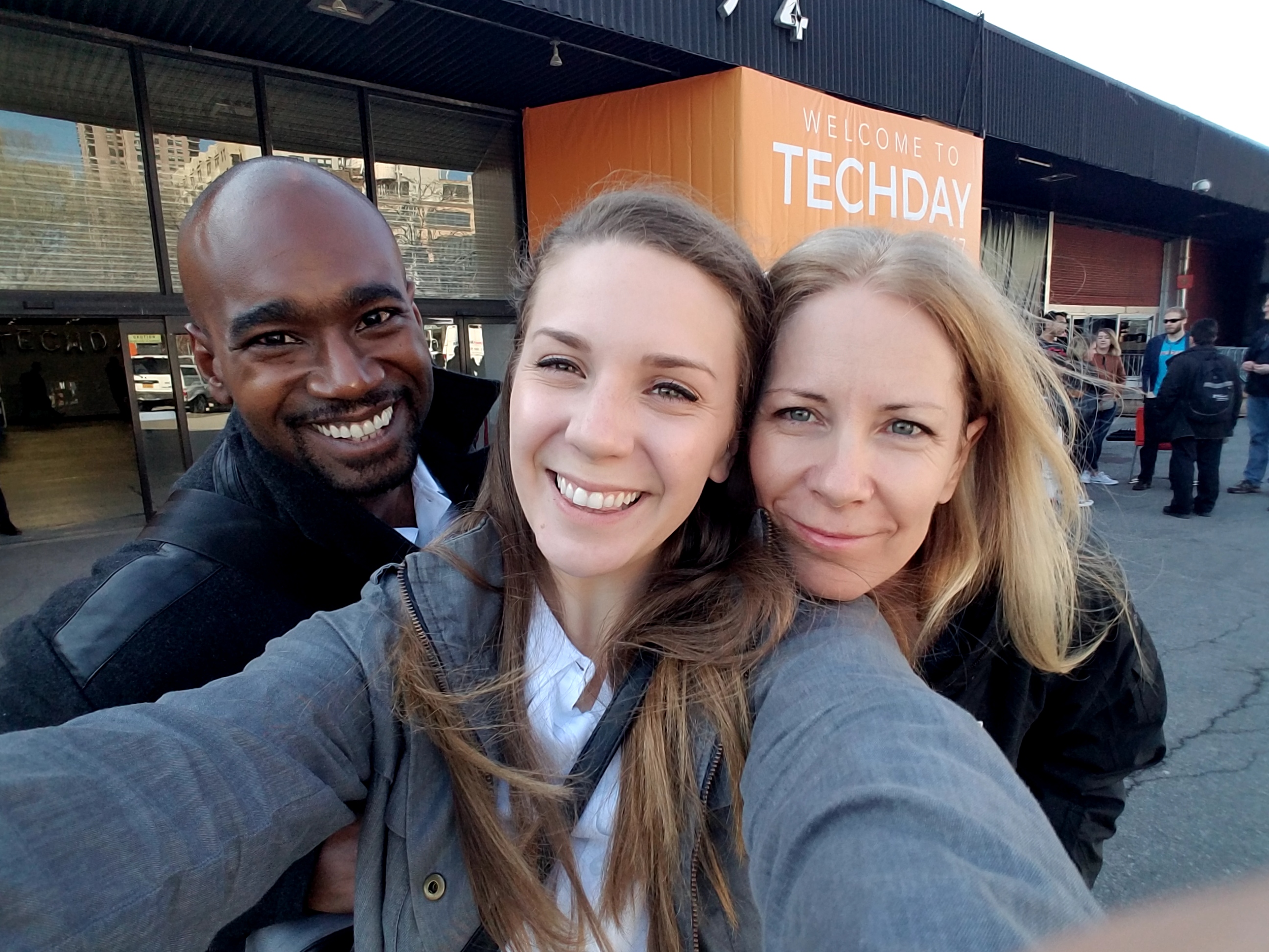 A male Minder and two female Minders take a selfie in front of a sign that says "Welcome To Techday."