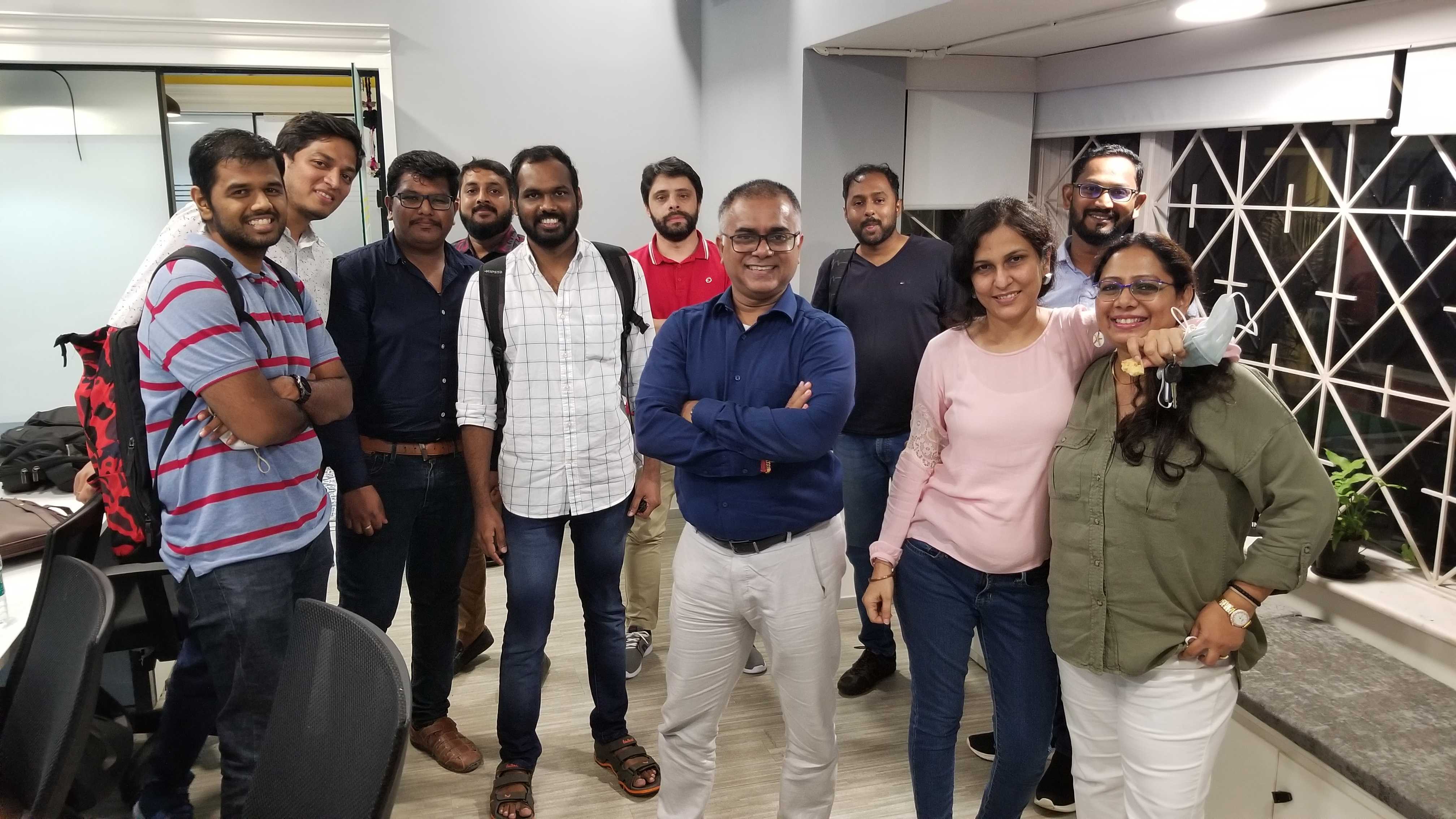 Nine male Minders and two female Minders pose for the camera and hug each other in the Mindera India office.