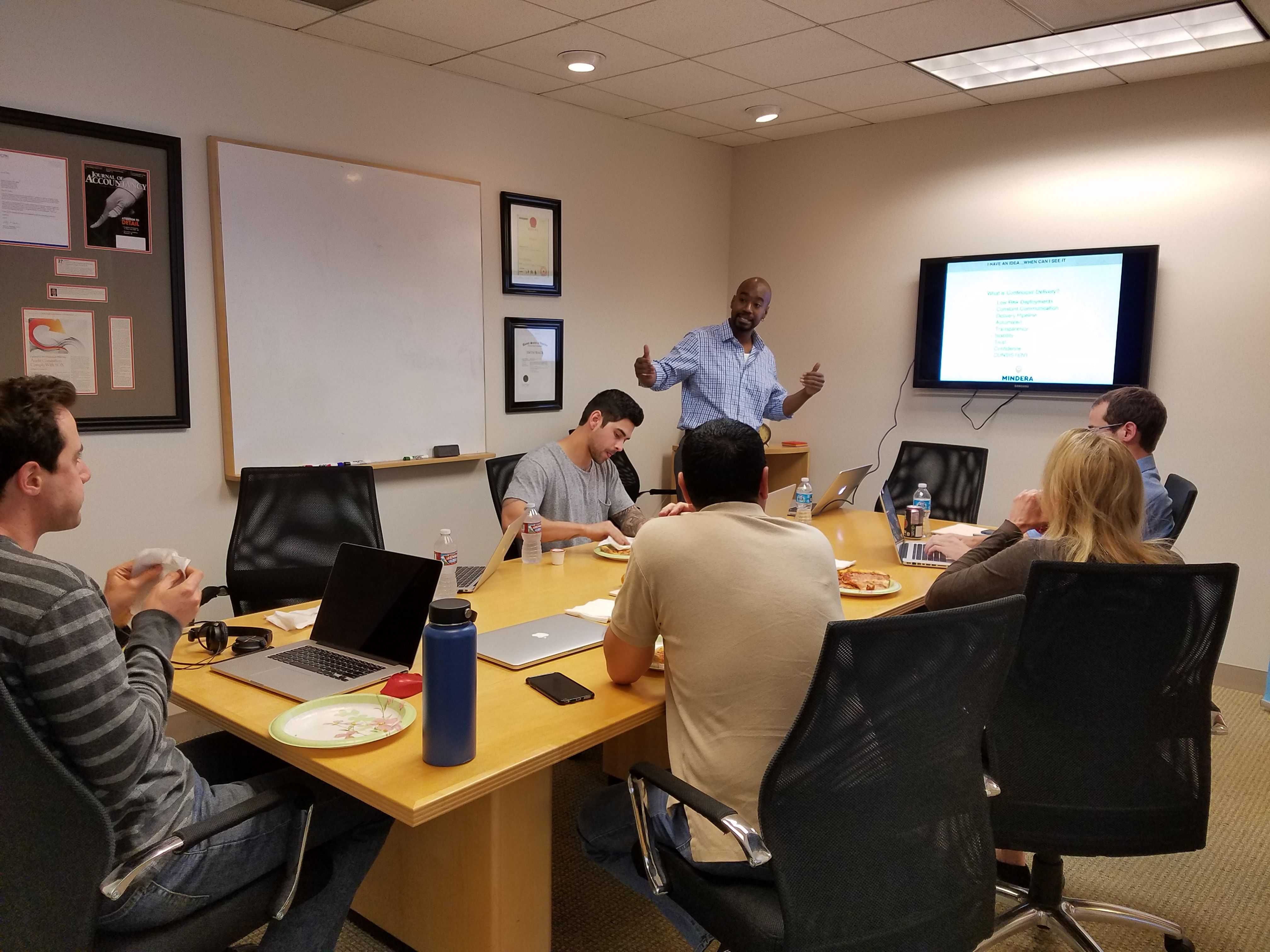 Five Minders are sat around a table as CJ presents a topic that's important for Mindera United States Minders.