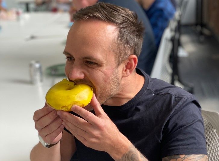 A man puts a doughnut into his mouth with both of his hands and eats it.