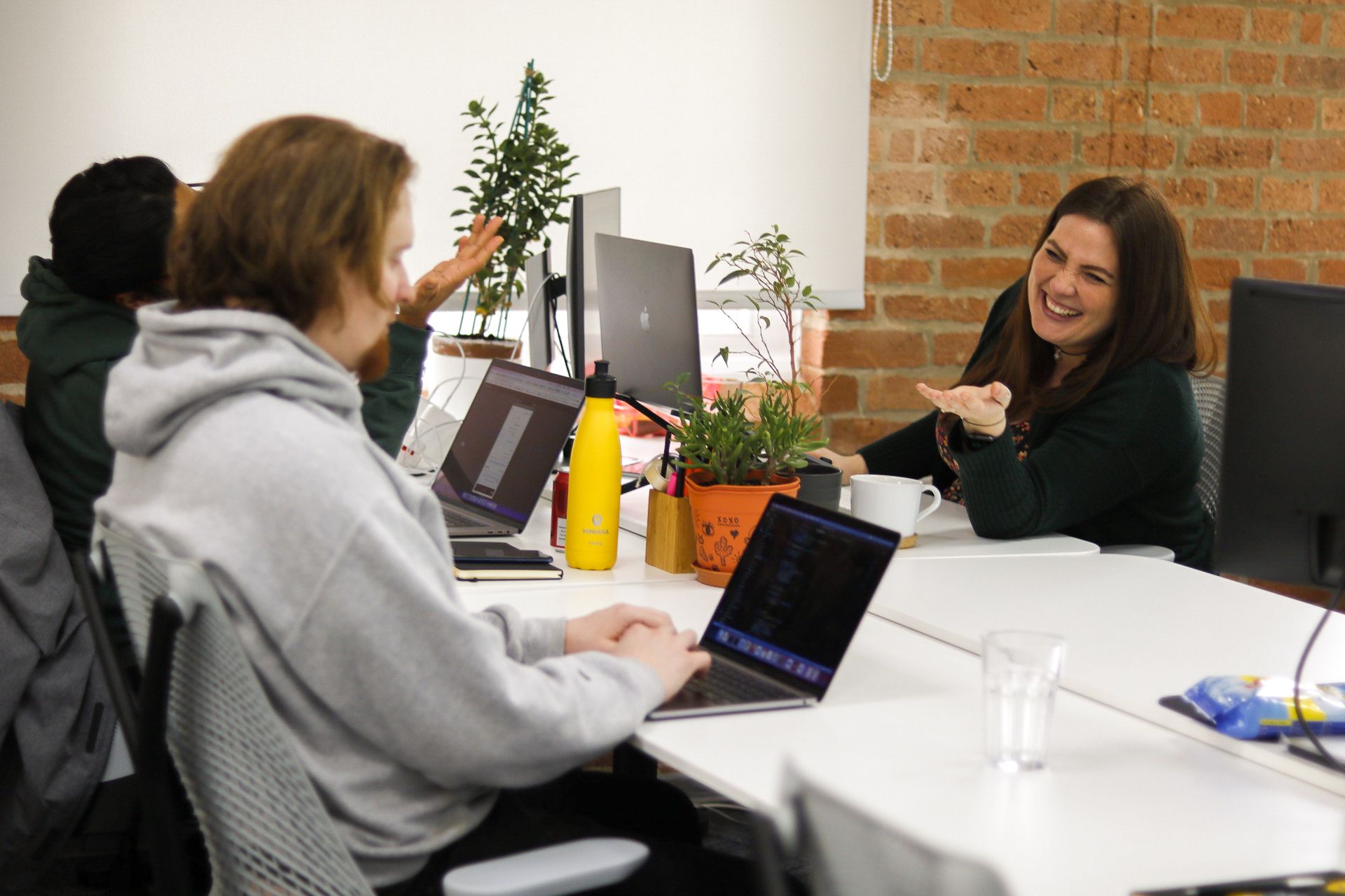 Three female Minders are laughing while working at their desks and laptops.