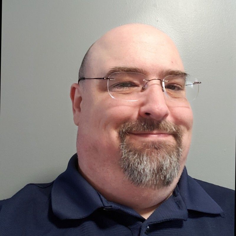 A man with a goatee beard and wearing glasses smiles at the camera. A man with a goatee beard and wearing glasses smiles at the camera.