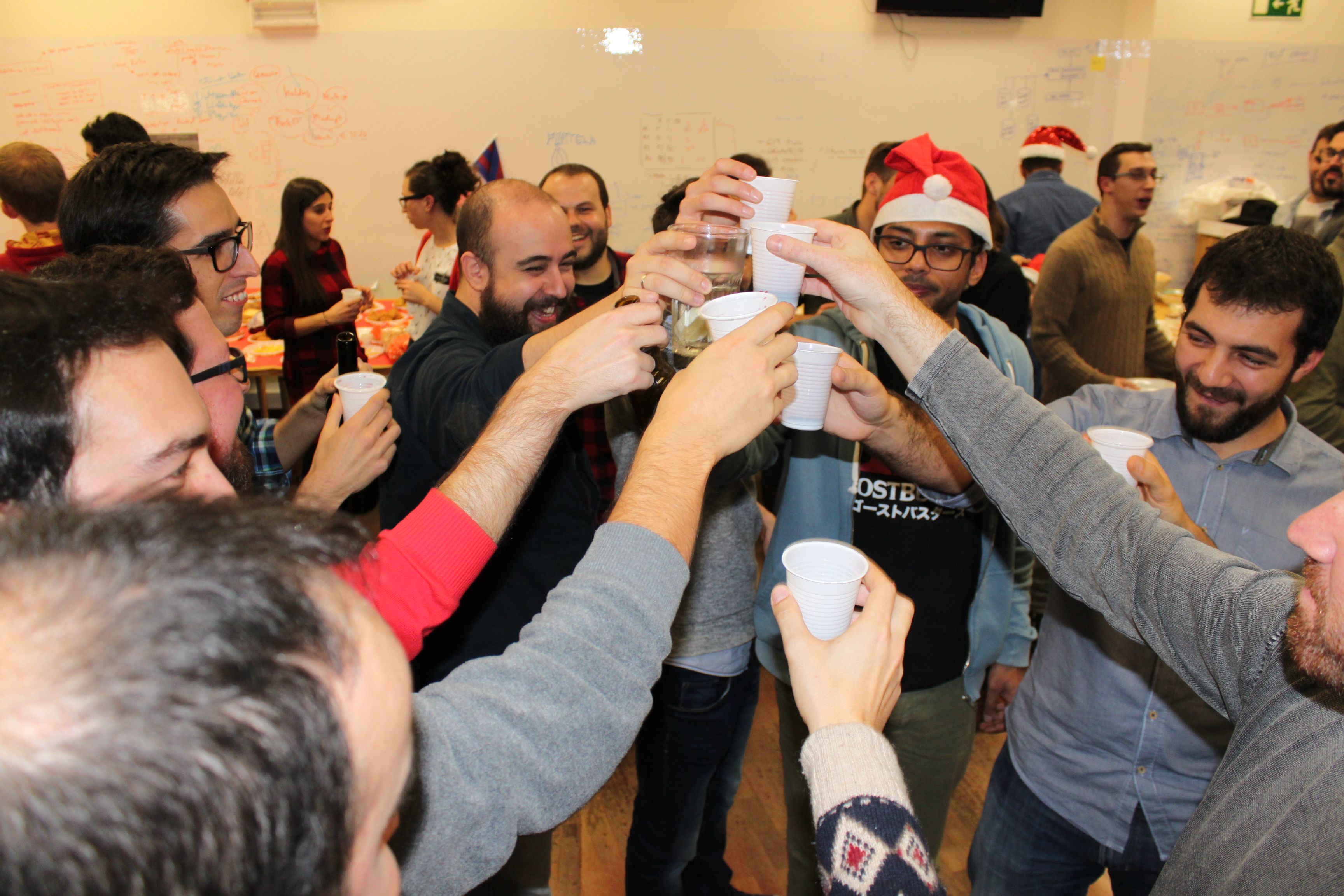 A group of Minders raise their glasses and plastic cups to cheers each other at the Christmas party for software engineering company Mindera. 