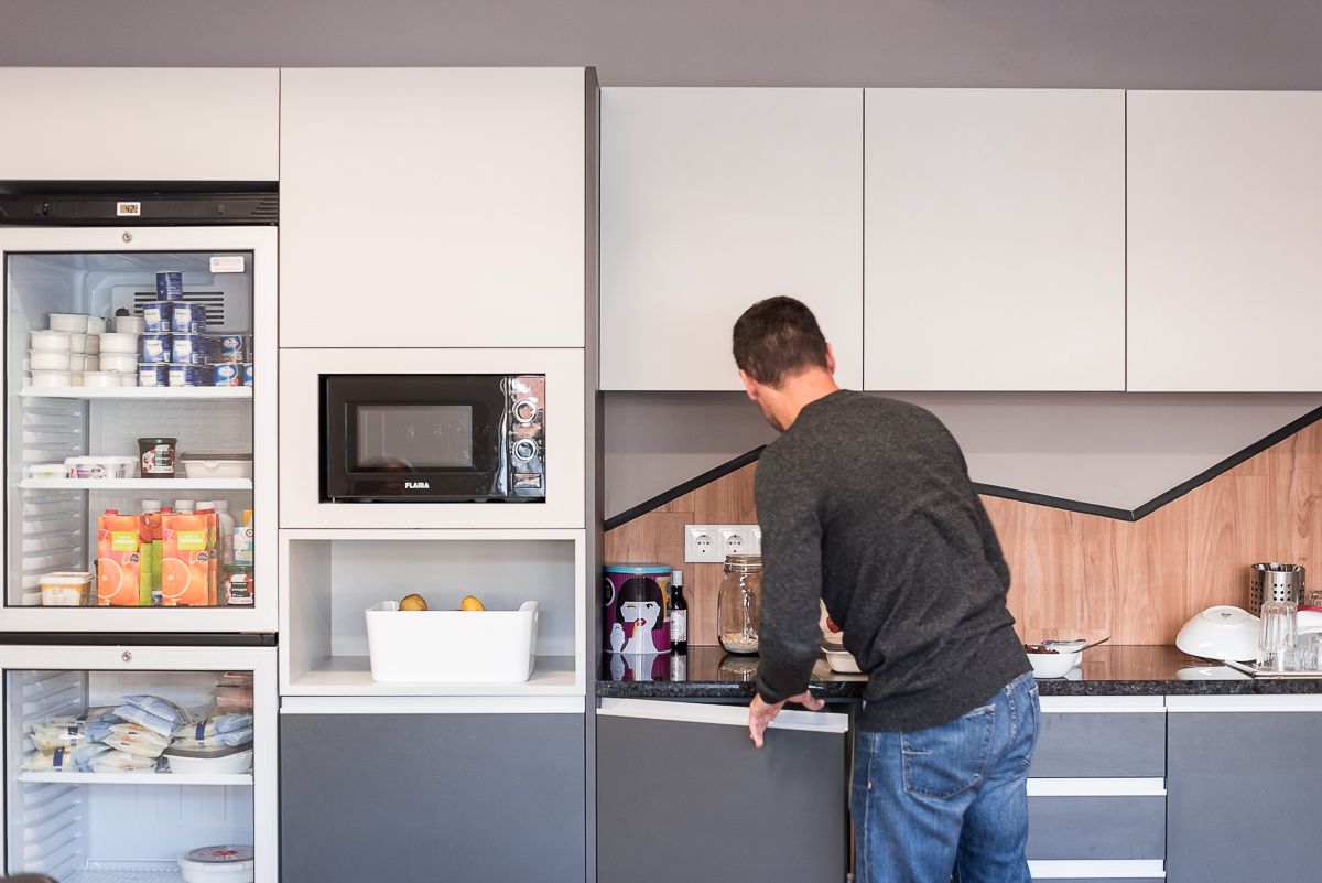 A male Minder wearing a grey jumper and blue jeans has his back to the camera as he gets some snacks from the kitchen in the Porto office of software engineering company Mindera. 