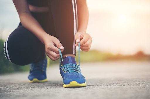 The arms, hands, legs, and feet of a female runner who is bending down to tie her shoelaces. 