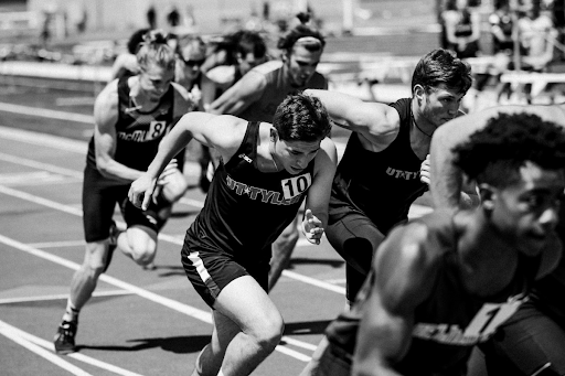 A black white image of eight male runners on a race track.