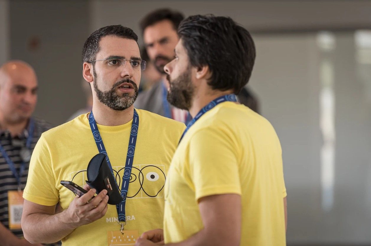 A photo of Tiago Pires, Backend Developer (Professional Juggler) for software engineering company Mindera, wearing a yellow t-shirt and talking to Ricardo Azevedo.