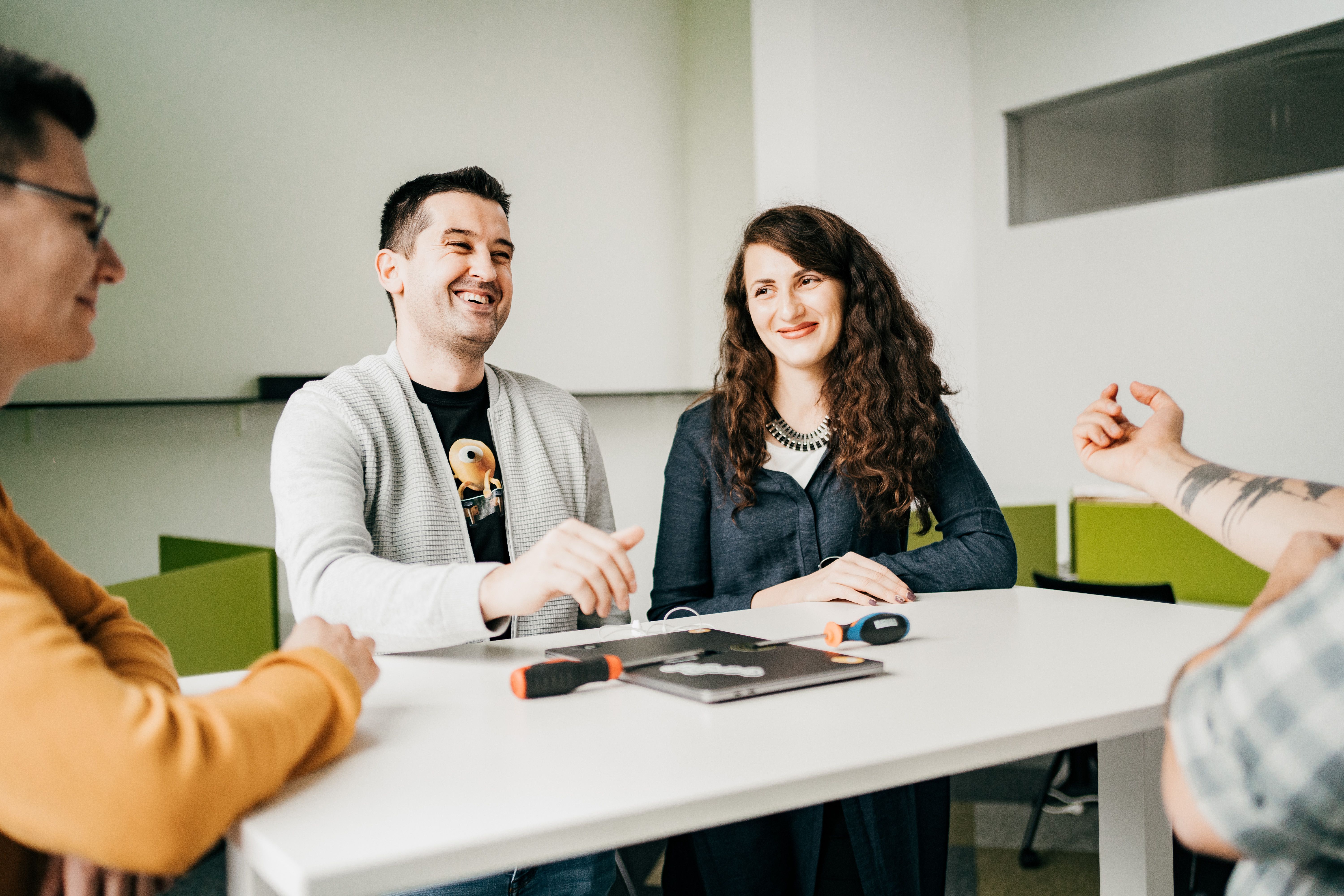 Four Minders are sat at a white table in the Mindera Romania office, smiling and talking about software engineering. 