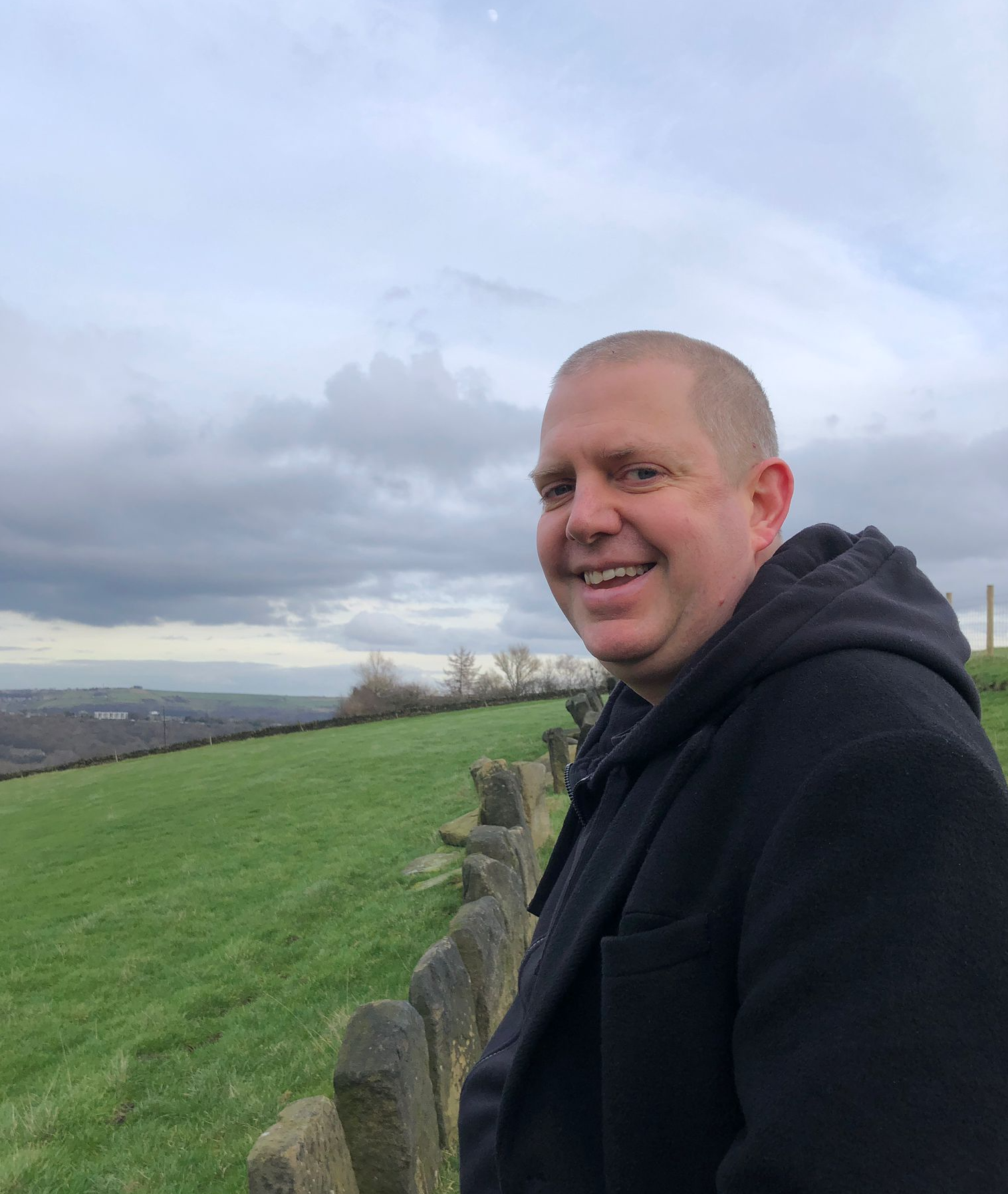 James Burt stands in profile on the moors and smiles at the camera. 