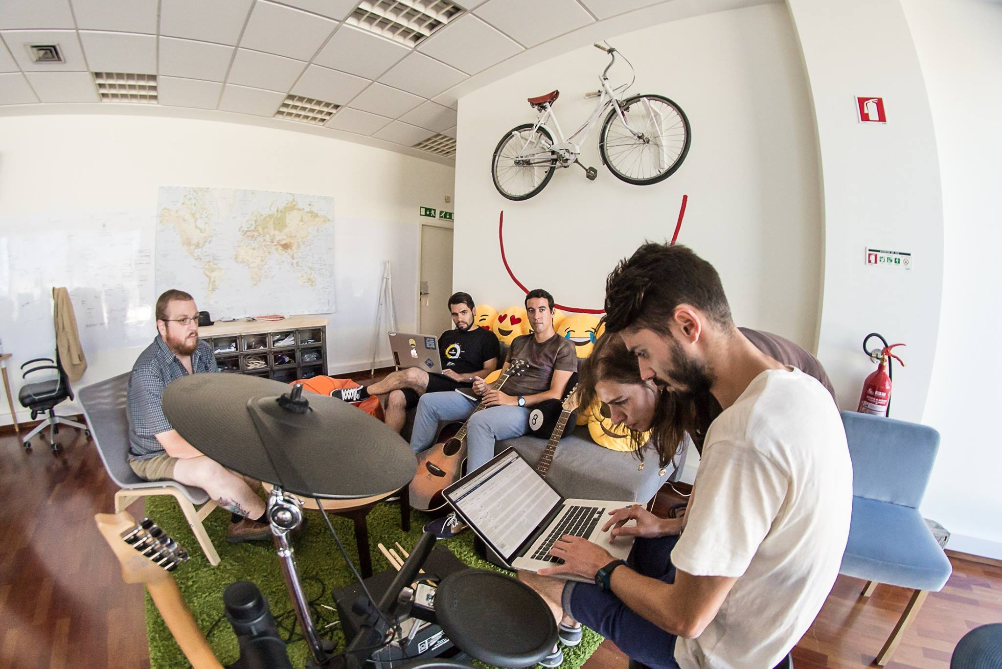 Five male Minders sit in a room full of musical instruments, with two of the Minders using a laptop to carry out software development work for the software engineering company Mindera. 