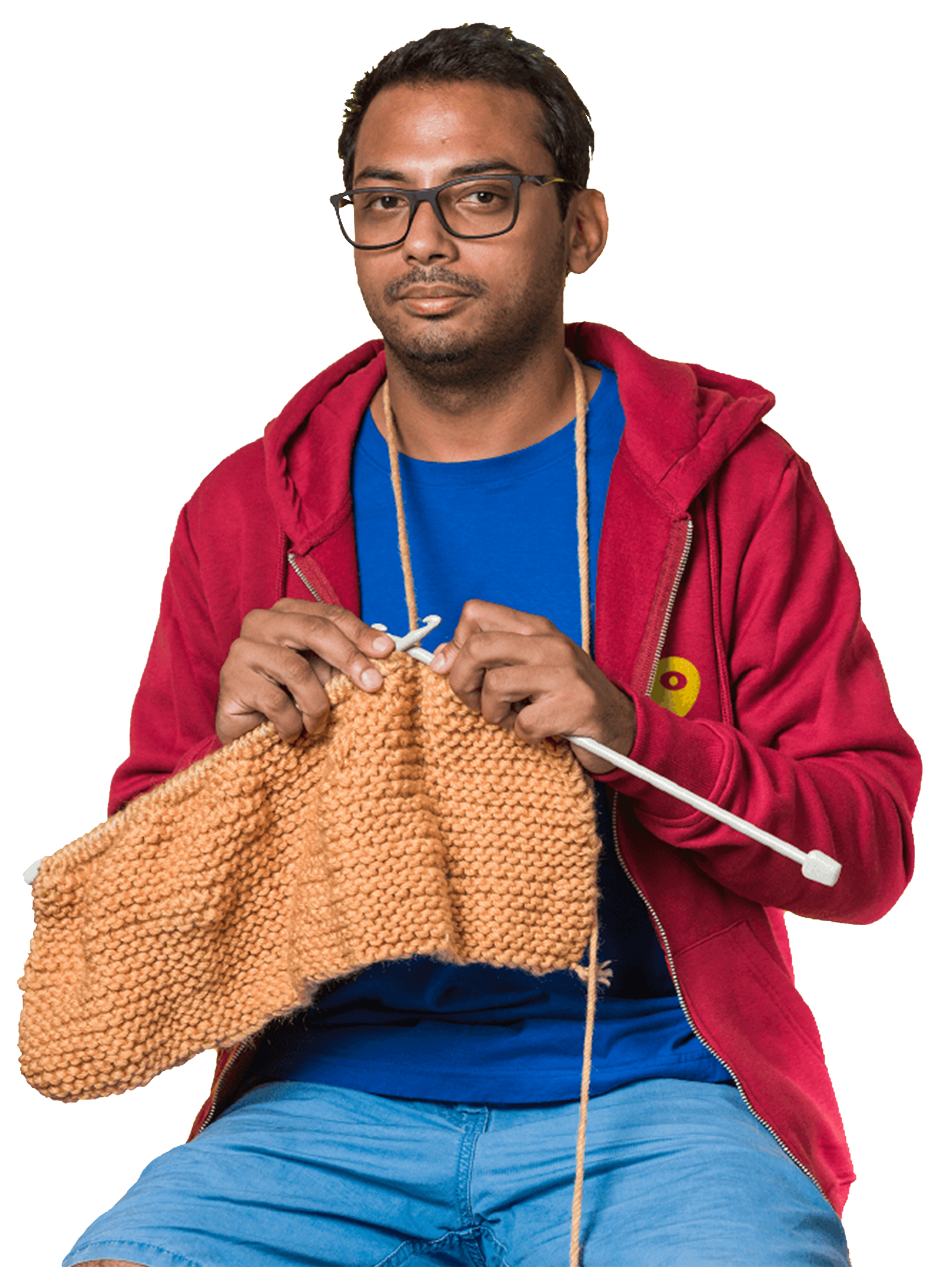 A male Minder wearing a red, unzipped hoodie with the Mindera logo on it faces the camera as he knits. 