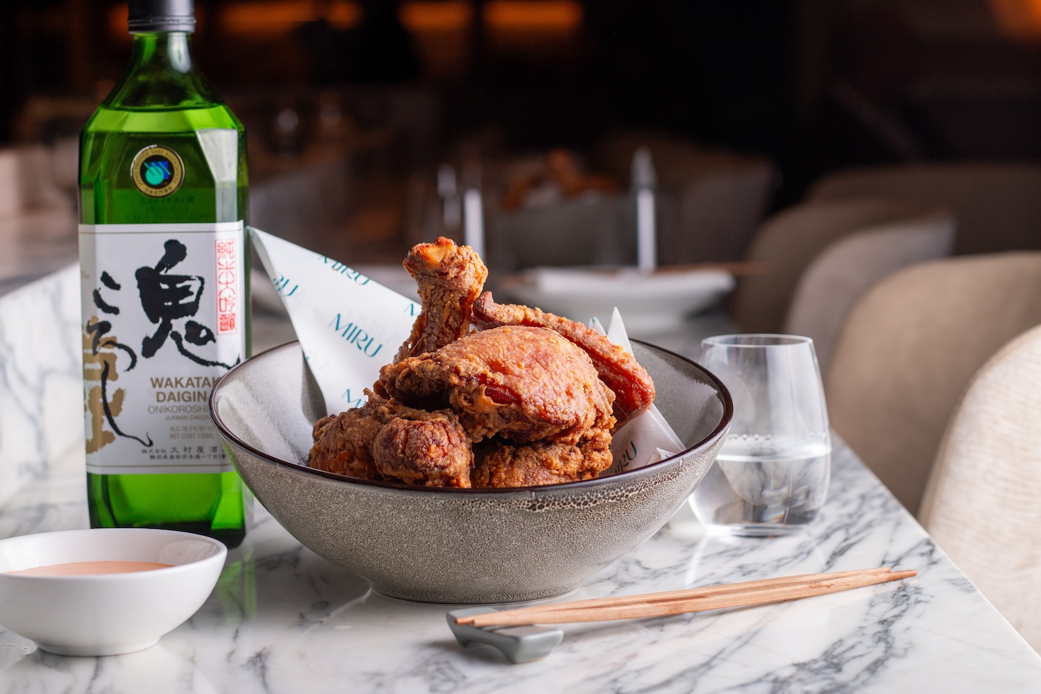 Japanese fried chicken on a marble counter with a bottle of green sake.