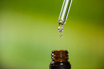 Drop oil dripping from pipette into bottle essential oil