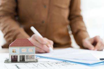 Realtor signing contract on clipboard next to miniature house