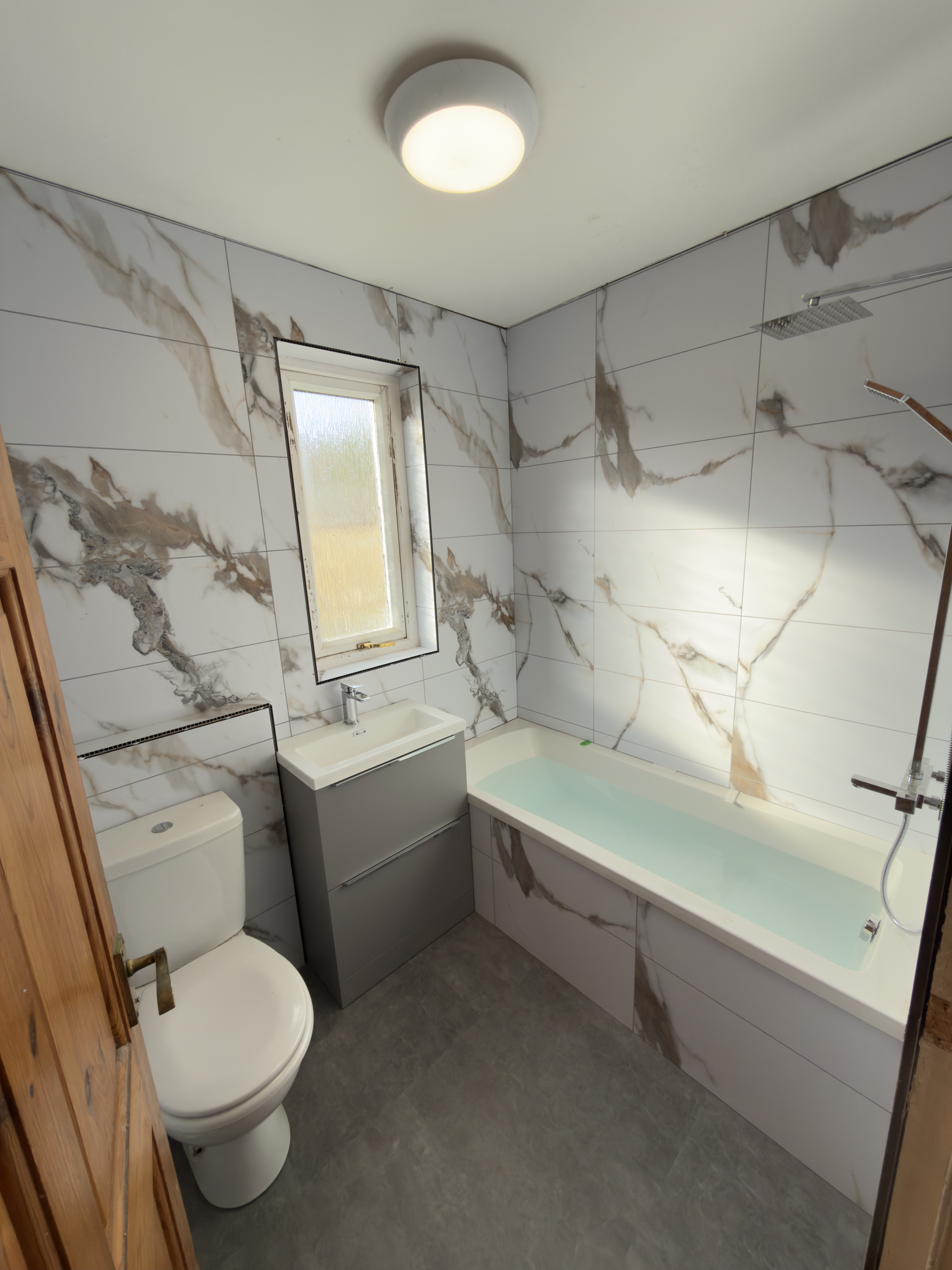 Newly renovated bathroom with Calcutta Gold wall boards, modern fixtures, and a grey vanity unit.
