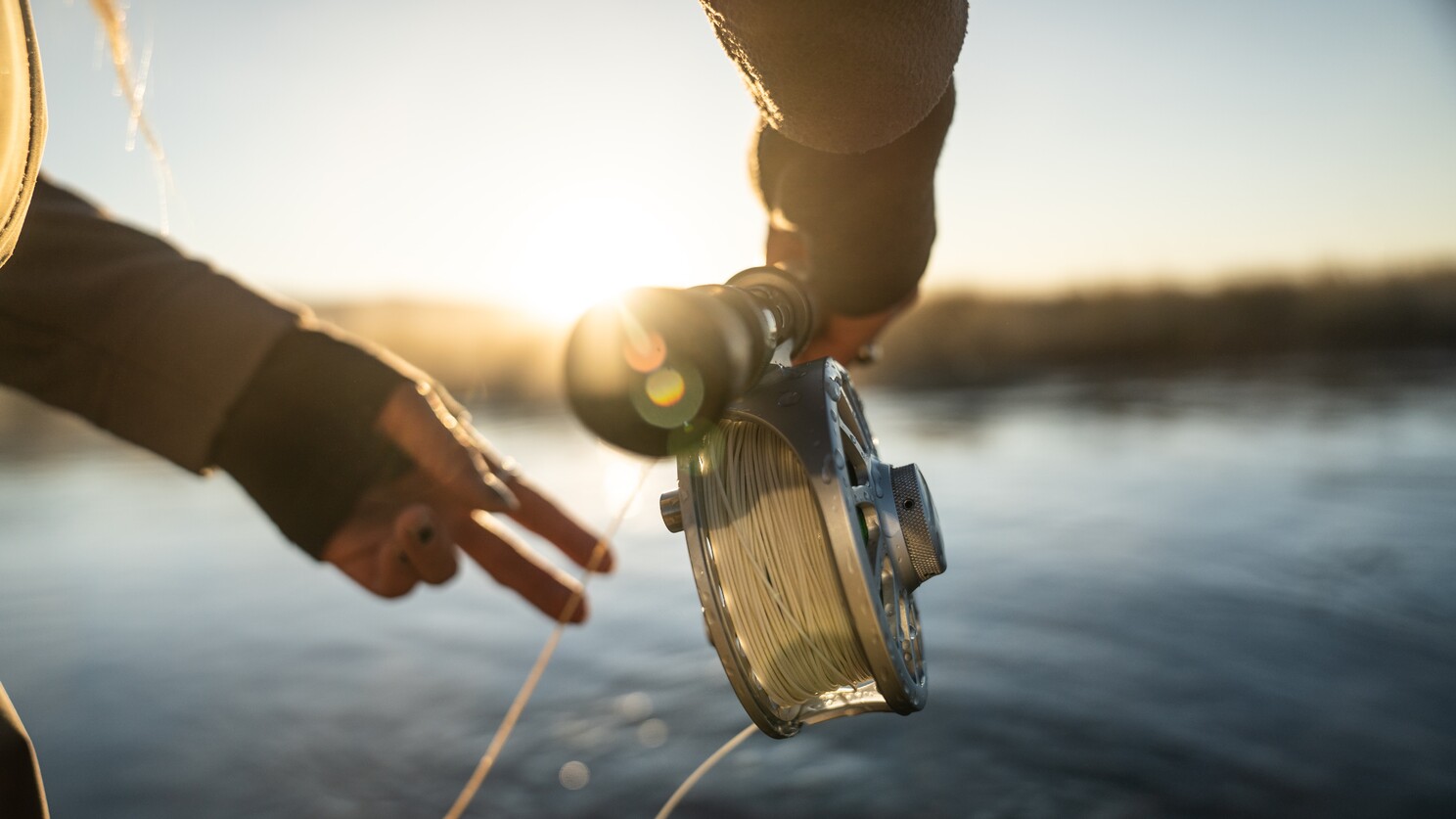 Close-up of a person holding a fishing reel with water in the background