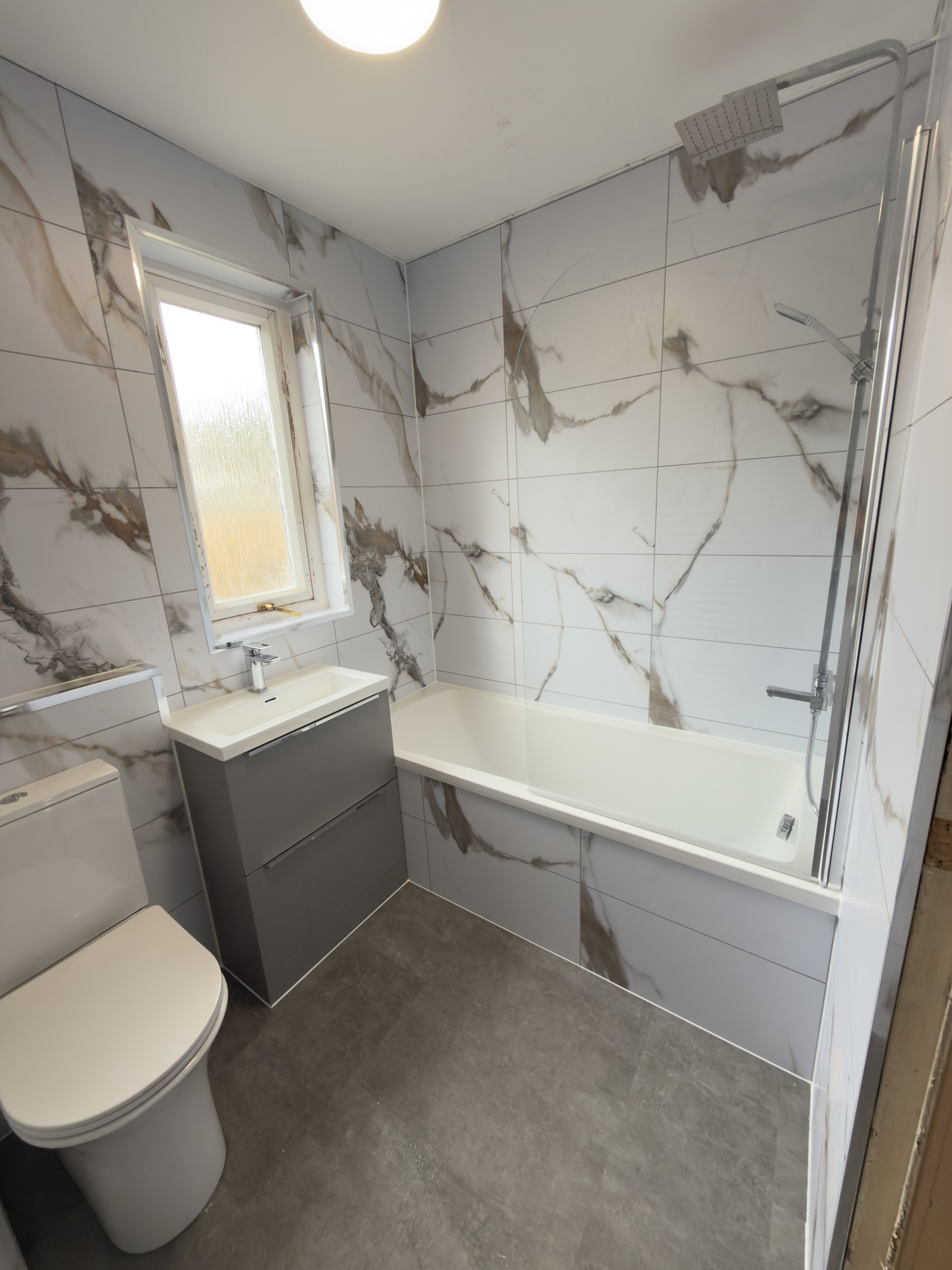 Bathtub and wash basin with tile effect walls.