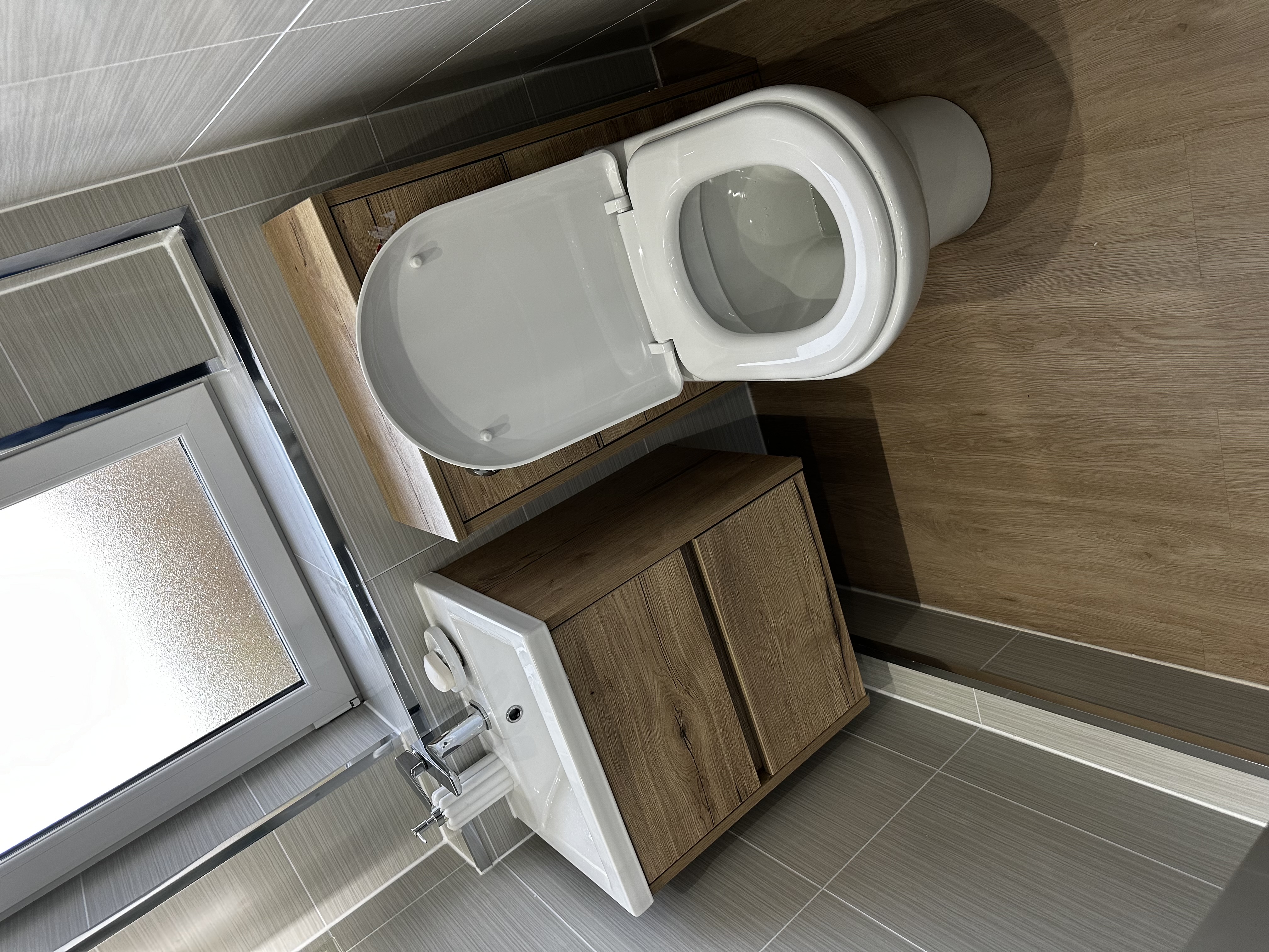 Close-up of oak vanity and toilet beneath a window.