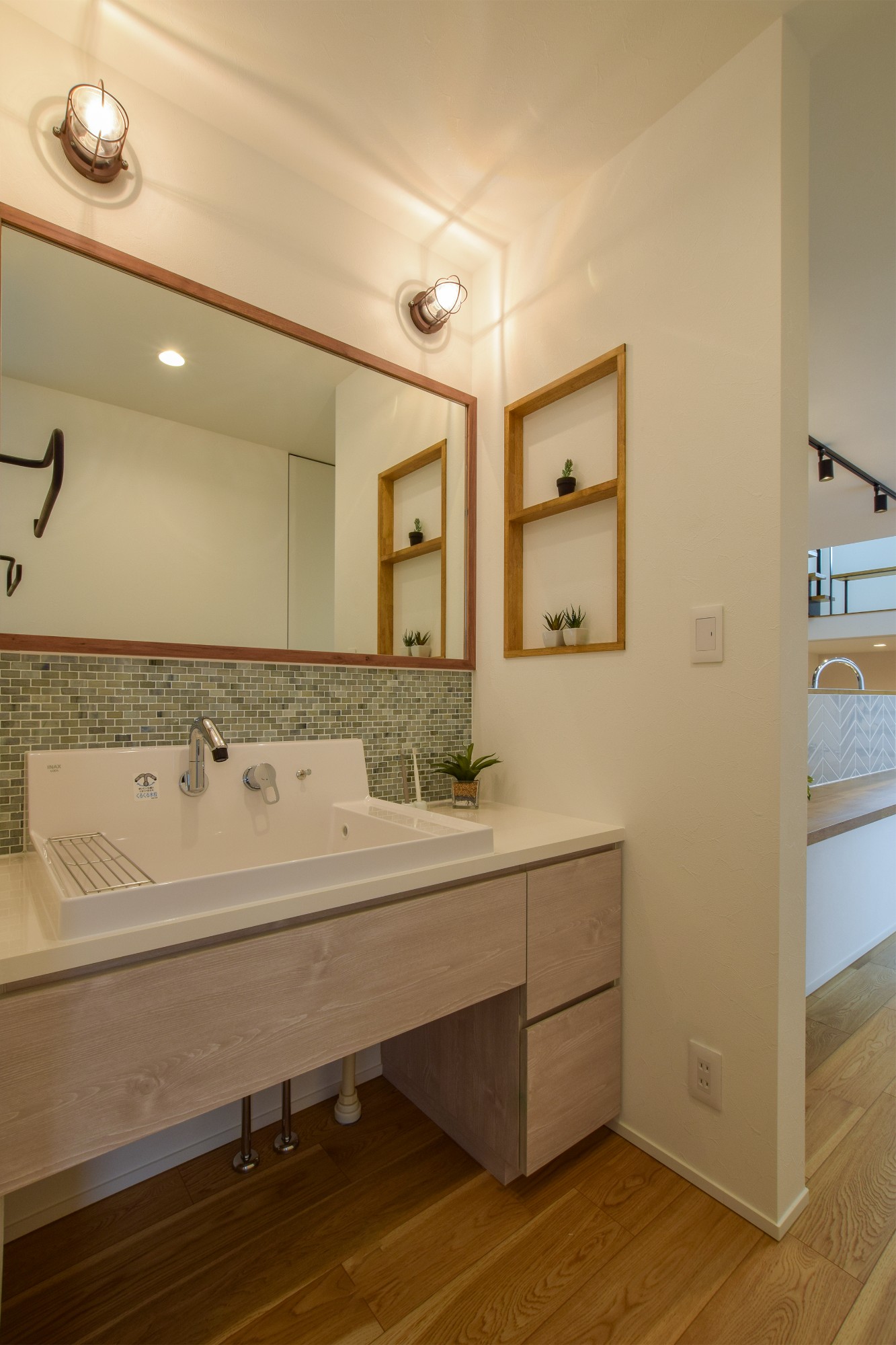 洗面台は大きな一面鏡で二人並んで使えるブルーグレーのガラスのタイルとマリンライトで爽やかさを演出。
