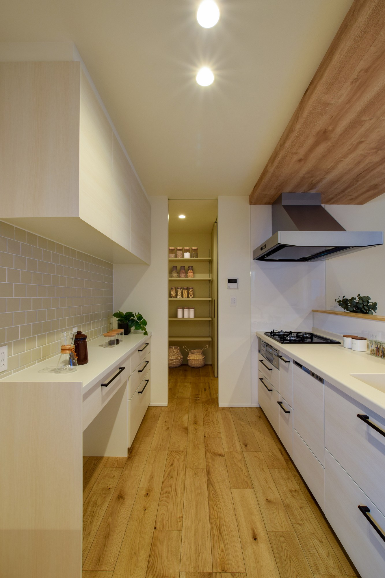 白の木目のキッチンとカップボードに、アイボリーのタイルがアクセントになった明るいキッチン。キッチンとカップボードの距離を十分に確保し、2人並んでもゆったりと作業ができる