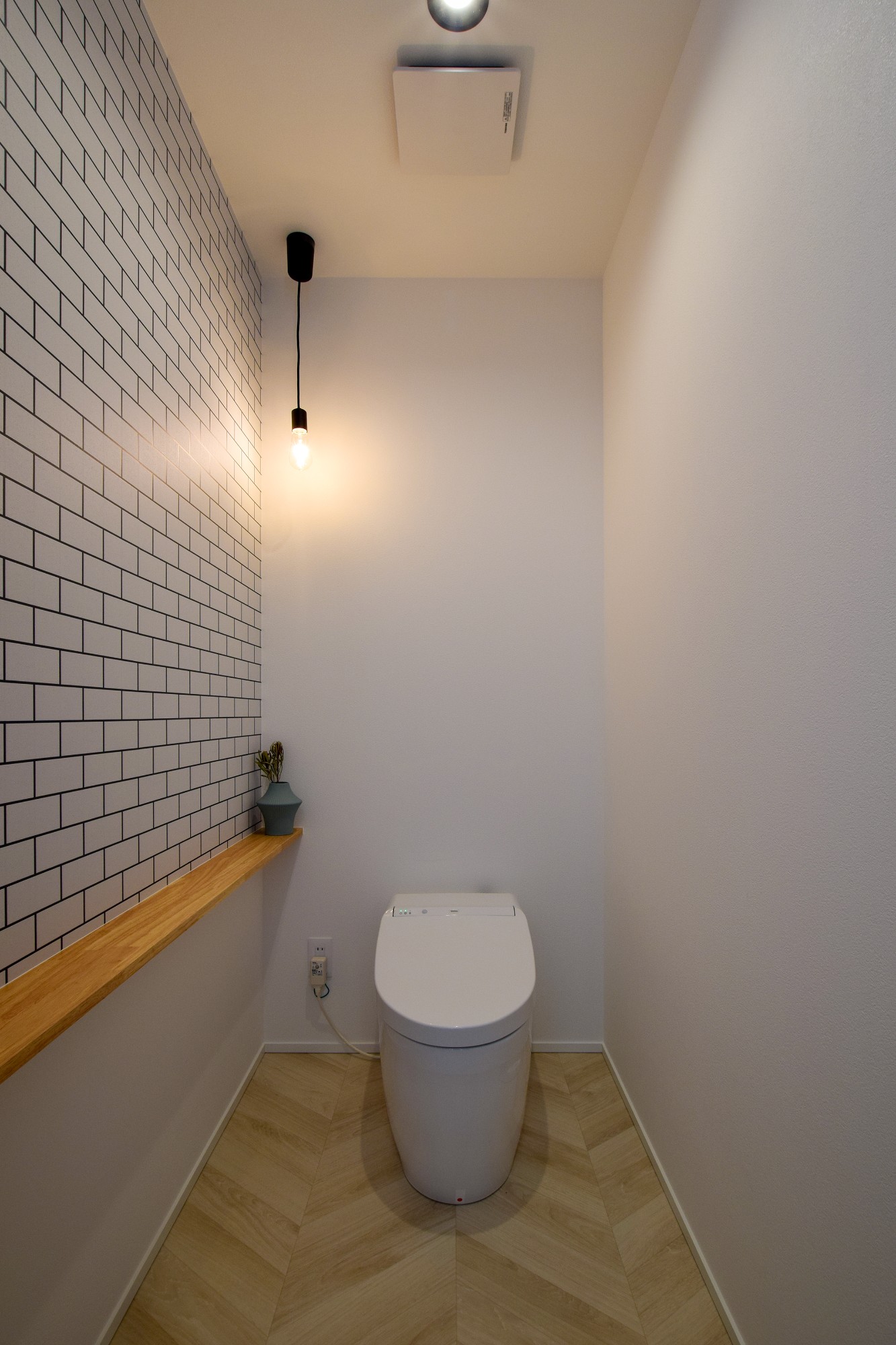 タイル調のアクセントクロスと、ヘリンボーンの組み合わせでカントリーな雰囲気のトイレ空間。ペンダントライト照明がいい雰囲気を醸し出す