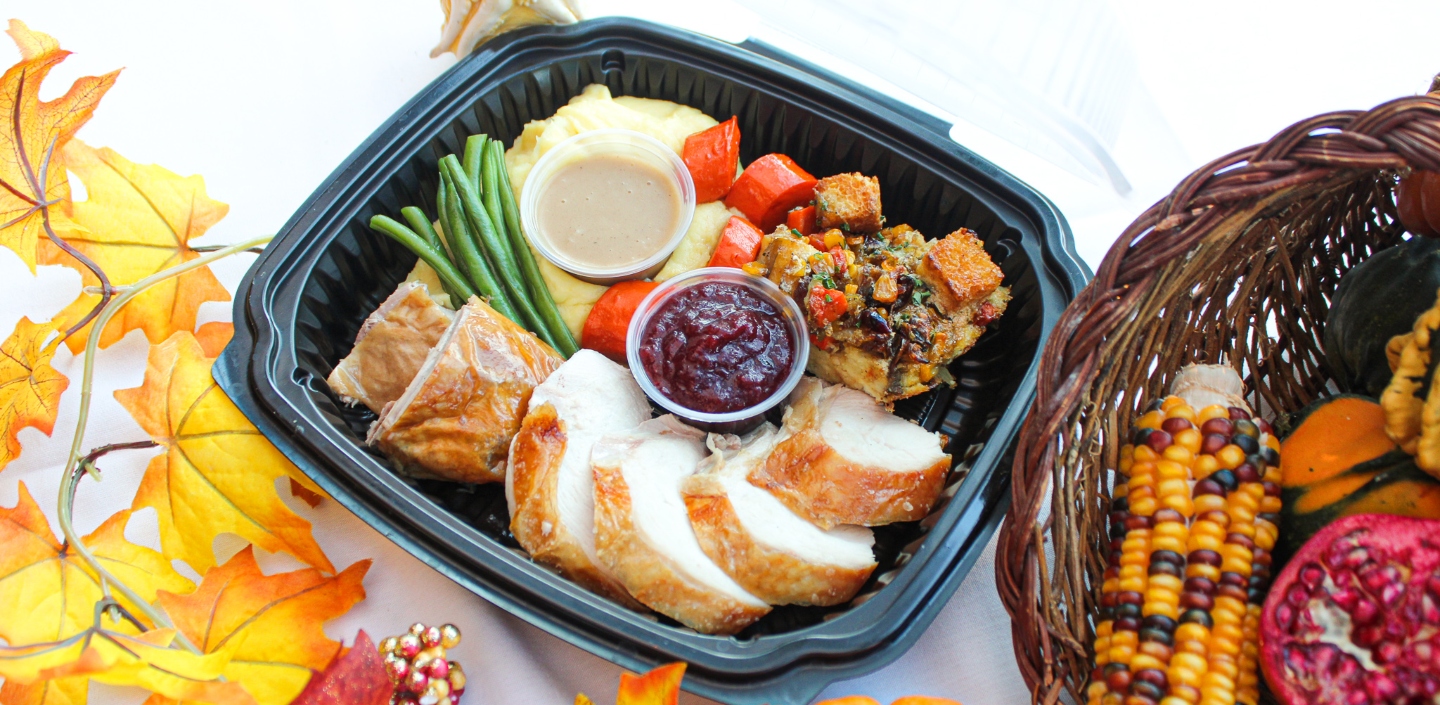 Mon Ami Gabi's Thanksgiving To-Go packed with turkey, cranberry sauce, stuffings, and greens, next too fall decorations and produce.