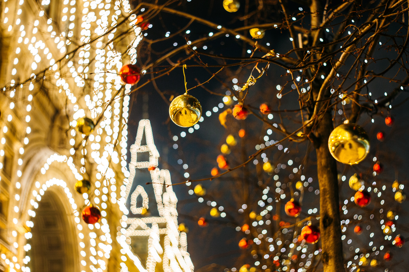 A tree adorned with ornaments and a house lit up with lights