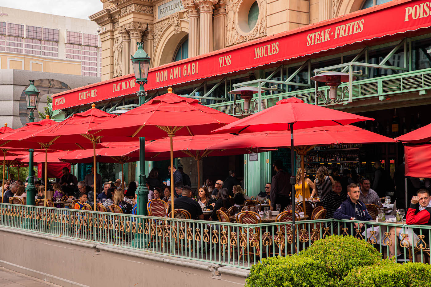 Photo of guests dining at Mon Ami Gabi on the patio with its red umbrellas opened.