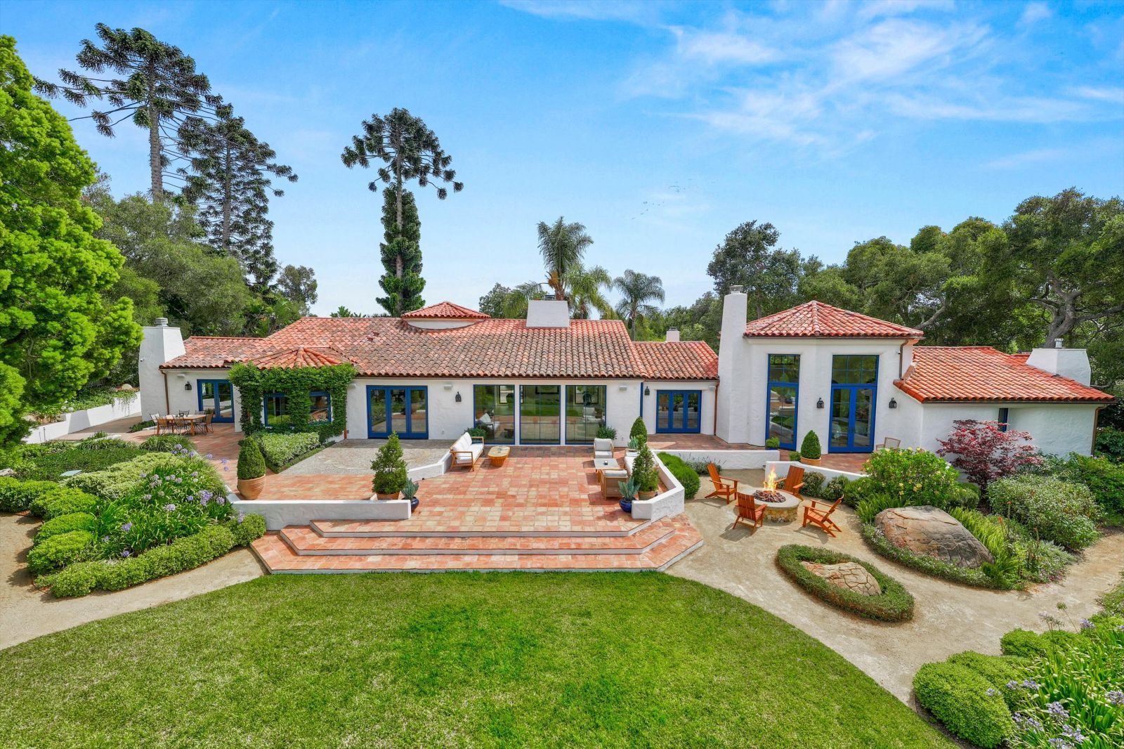 A classic hacienda style single-story home with a red tile roof, with sprawling lawn and tiled terrace in the foreground.