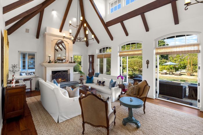 The great room of a luxury home with wood beamed and vaulted ceiling and the sun streaming through multiple windows and french doors.