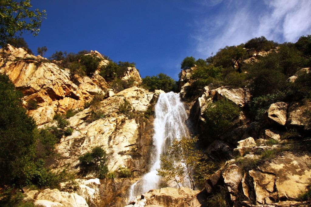 A significant waterfall cascading over, and down a rock wall glowing in the sunlight.