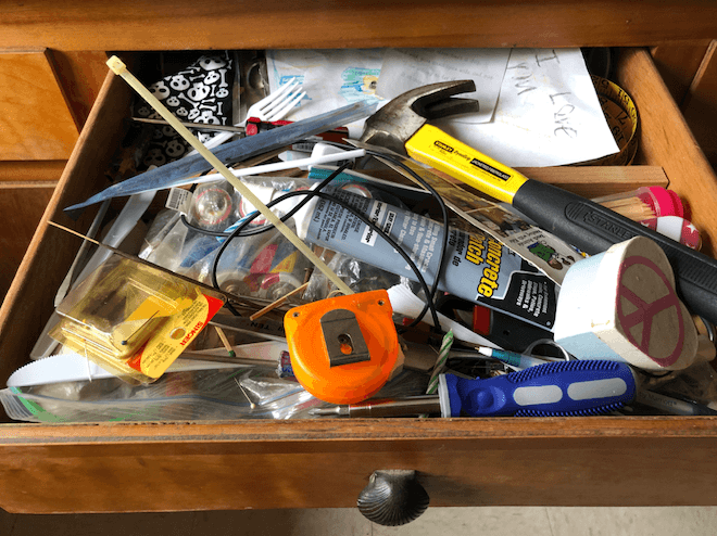 Typical junk drawer with a lot of misc stuff including a hammer and other tools
