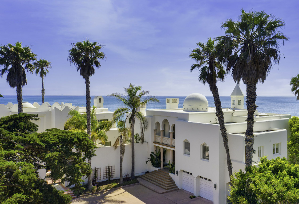 A birds eye view of A Lavish California Beach Villa that's currently on the market surrounded by palm trees with the blue ocean in the background