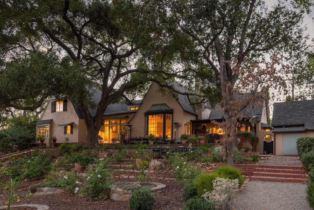 The front of a story book looking estate in Ojai, Calfiornia taken at night with twinkling lights in the windows. The estate is surrounded by trees and shrubs.