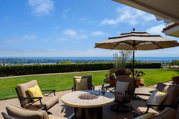 Backyard of a beautiful estate with patio furniture and umbrella looking out to the ocean