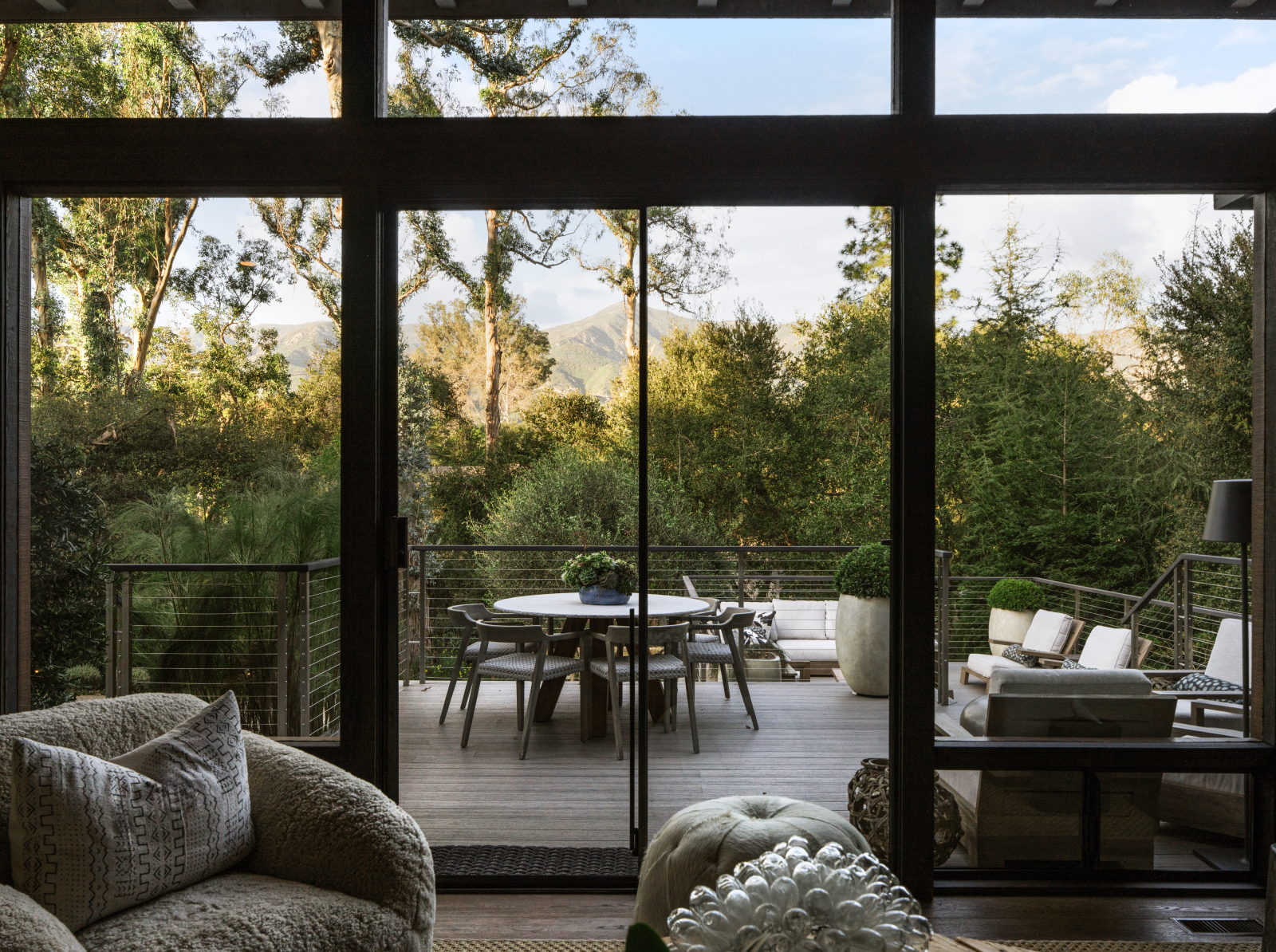 Indoor-outdoor living space in a Santa Barbara home with sliding glass doors opening to a private deck, dining area, lounge seating, and serene mountain and tree views